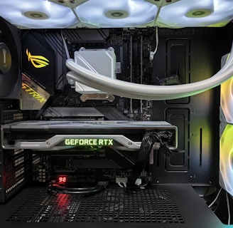 Inside view of a computer case showcasing a sophisticated gaming setup. Visible components include a GeForce RTX graphics card illuminated with green lighting, an ASUS motherboard, cooling fans with LED lighting, and a liquid cooling system with white tubes. Cables are neatly organized, and overall, the hardware suggests a high-performance machine.