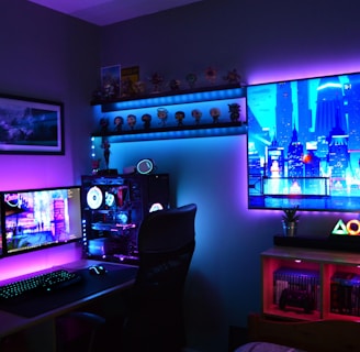 A vibrant gaming setup featuring multiple monitors displaying a cyberpunk cityscape. The room is illuminated with neon purple and blue LED lights, adding a futuristic ambiance. A custom-built PC with glowing components sits to the side, and shelves with collectible figurines are visible. A large digital screen on the wall shows an animated city scene, enhancing the immersive atmosphere.